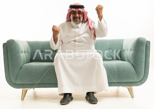 رجل سعودي يحتفل بالنجاح على أريكة بخلفية بيضاء