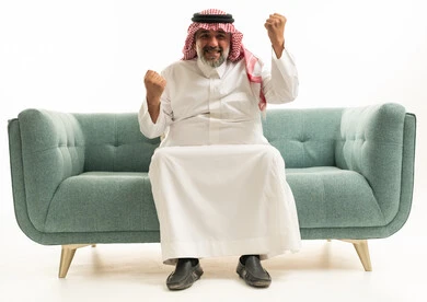 رجل سعودي يحتفل بالنجاح على أريكة بخلفية بيضاء
