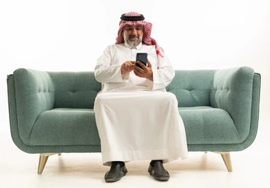 Saudi Man in Traditional Thobe Using Smartphone on Sofa