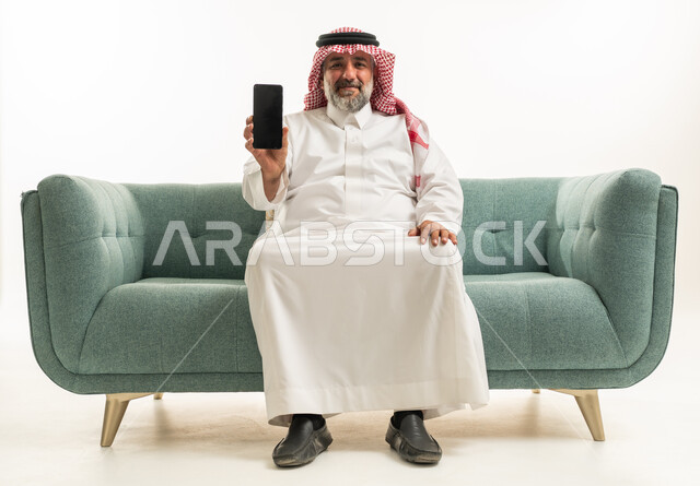 رجل سعودي يحمل هاتف ذكي على أريكة خضراء في استوديو