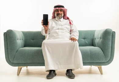 رجل سعودي يحمل هاتف ذكي على أريكة خضراء في استوديو