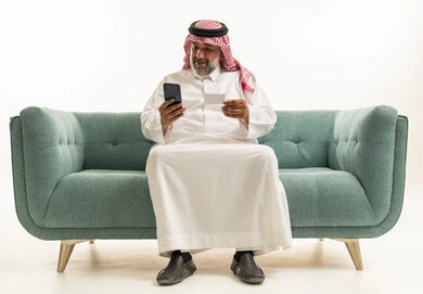 رجل سعودي يستخدم الهاتف والبطاقة الائتمانية على الأريكة