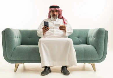 Saudi Man Using Smartphone and Credit Card on Sofa