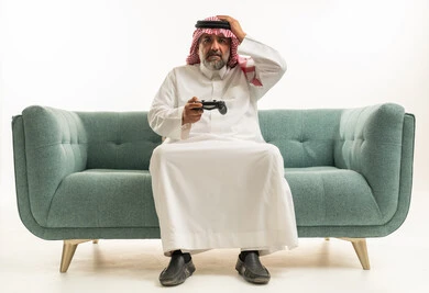 رجل سعودي مسن يلعب ألعاب الفيديو على الأريكة