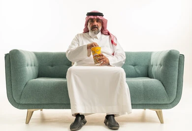 رجل سعودي بالثوب التقليدي يأكل الفشار على الأريكة