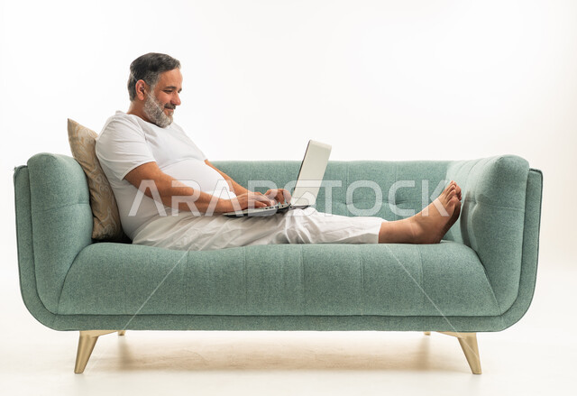 رجل عربي يستخدم المحمول على أريكة بخلفية بيضاء