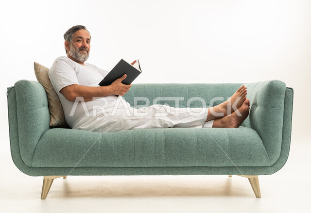 رجل هندي يقرأ كتاباً على أريكة خضراء في استوديو خلفية بيضاء