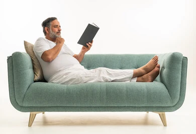 رجل سعودي يقرأ كتاباً على أريكة خضراء بخلفية بيضاء