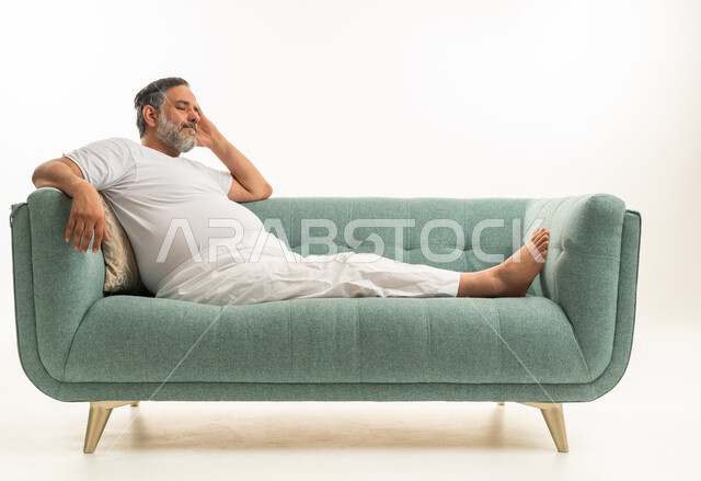 رجل سعودي خمسيني مستلقي على أريكة بملابس بيضاء