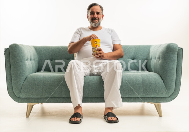 رجل سعودي يأكل الفشار على أريكة خضراء