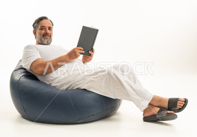 رجل سعودي يقرأ كتاباً على مقعد بين باج أزرق