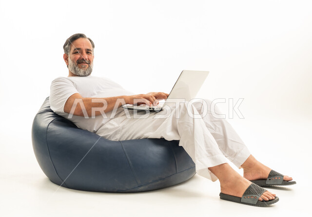 رجل عربي يستخدم اللابتوب على مقعد محشو في استوديو
