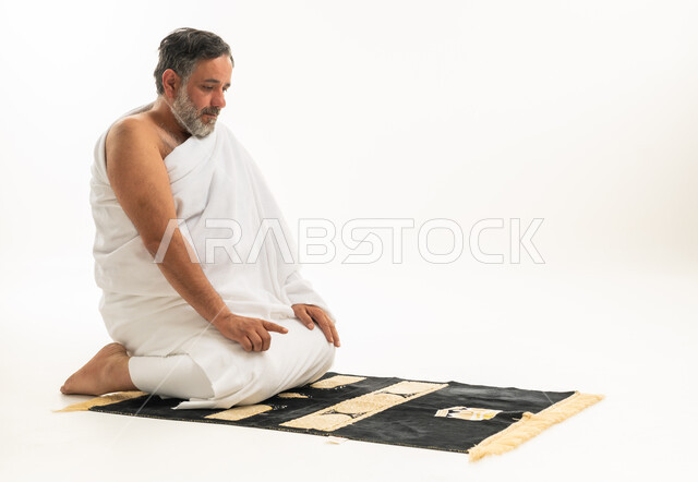 رجل سعودي بملابس الإحرام يصلي على خلفية بيضاء