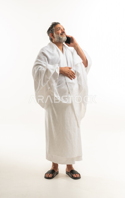رجل عربي بملابس الإحرام يتحدث بالجوال خلفية بيضاء