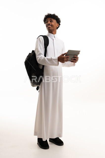 طالب سعودي بالثوب التقليدي يحمل جهاز لوحي وحقيبة