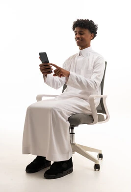 شاب سعودي بالثوب يستخدم الهاتف الذكي على كرسي مكتب