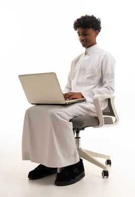 شاب سعودي بالثوب الأبيض يستخدم المحمول على كرسي مكتب