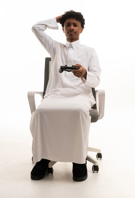 شاب سعودي بالثوب يمسك جهاز تحكم ألعاب بخلفية بيضاء