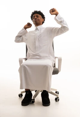 رجل سعودي يرتدي الثوب يمتد على كرسي مكتب بخلفية بيضاء