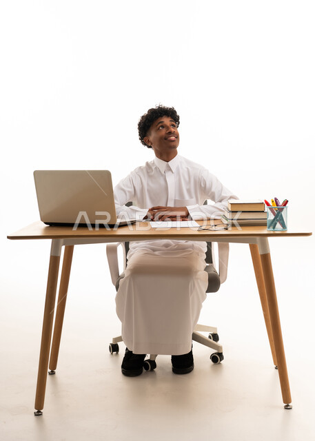 طالب سعودي جالس خلف مكتب مع لابتوب بخلفية بيضاء