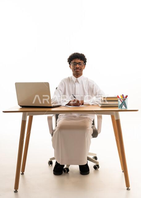 شاب سعودي بالثوب التقليدي يكتب على مكتب دراسي