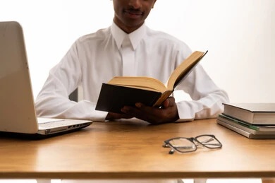 Saudi Man Reading Book at Desk with Laptop