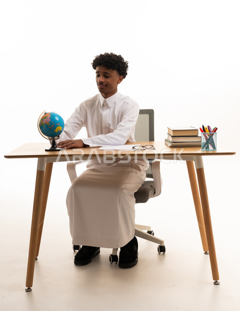 شاب سعودي مع مجسم كرة أرضية على مكتب الدراسة