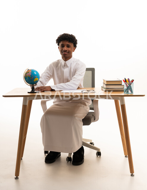 طالب سعودي يجلس على مكتب مع كرة أرضية