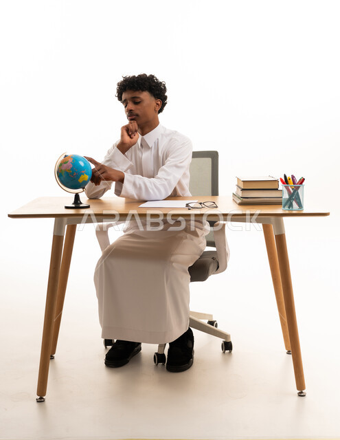 طالب سعودي بالثوب يدرس الكرة الأرضية على المكتب