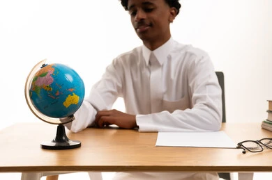 Saudi Student in Thobe at Desk with Globe