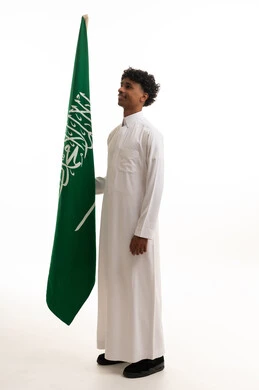 رجل سعودي بالثوب الأبيض مع العلم الوطني السعودي