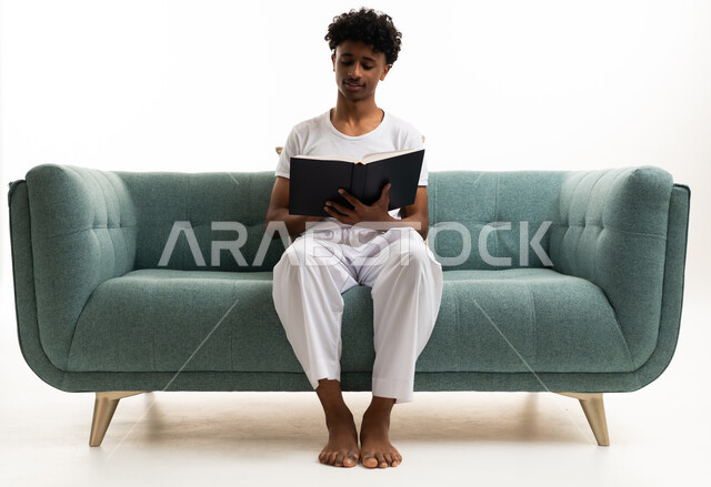 شاب سعودي يقرأ كتاباً على أريكة خضراء