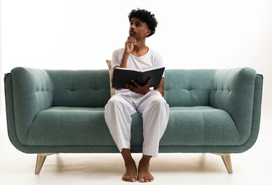 Saudi Man in White Loungewear Thinking with Book on Sofa