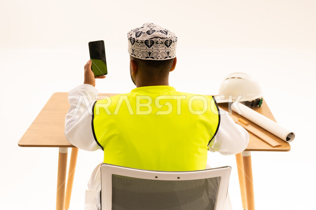 مهندس عماني يمسك هاتف بشاشة خضراء خلف مكتبه
