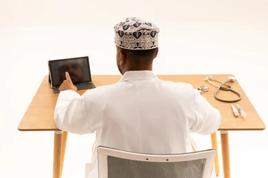 Omani Doctor at Desk Using Tablet Back View