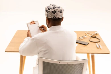 Omani Doctor Writing on Clipboard at Medical Desk