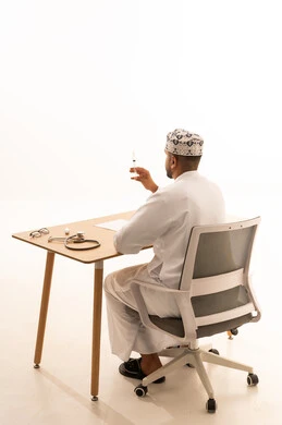 Omani Male Doctor Holding Syringe at Clinic Desk