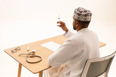 طبيب عماني يمسك حقنة طبية خلف مكتبه