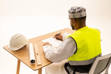 مهندس عماني يرتدي سترة السلامة ويكتب على مكتبه