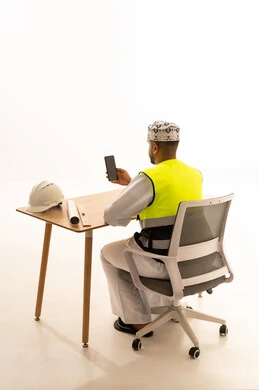 Omani Engineer with Safety Vest and Smartphone at Desk