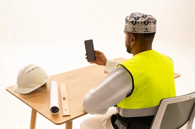 Omani Engineer in Safety Vest Using Smartphone at Desk