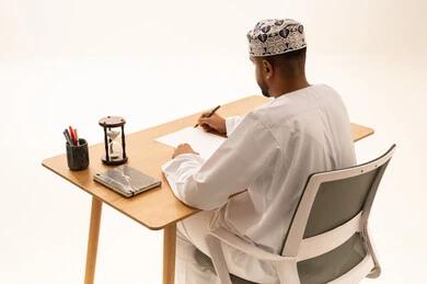 Omani Man Writing at Desk with Hourglass
