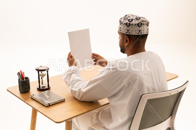 رجل عماني بالزي التقليدي يقرأ وثيقة على مكتب العمل