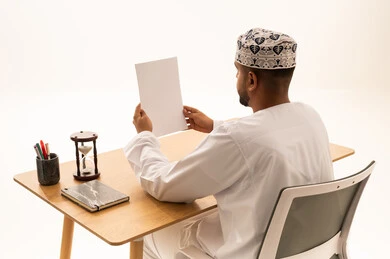 رجل عماني بالزي التقليدي يقرأ وثيقة على مكتب العمل