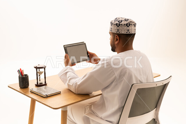 رجل عماني بالزي التقليدي يستخدم جهازاً لوحياً
