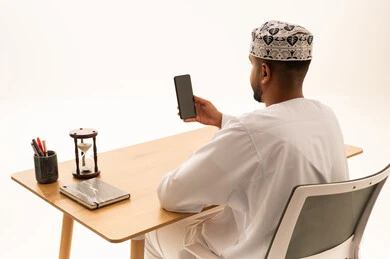 Omani Man at Desk with Smartphone and Hourglass