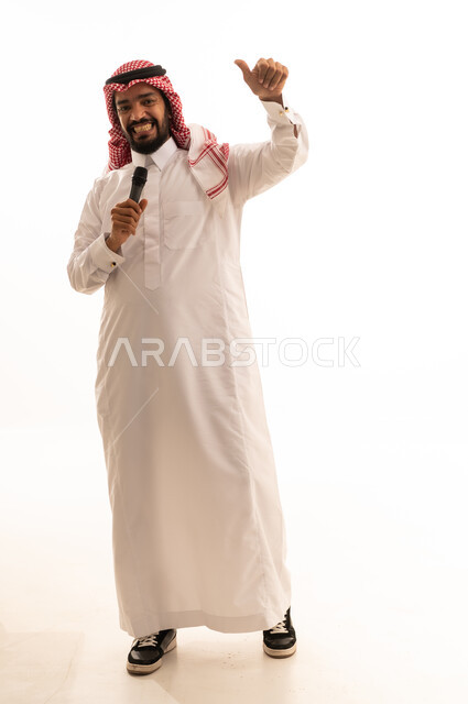 رجل سعودي بالثوب التقليدي يمسك ميكروفون وإشارة الإبهام
