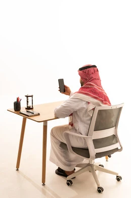 رجل سعودي يستخدم هاتف ذكي على مكتب عمل