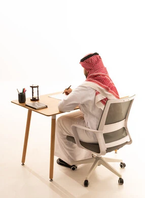 رجل أعمال سعودي يكتب على مكتبه بالزي التقليدي