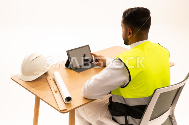 مهندس عربي يرتدي سترة السلامة مع جهاز لوحي على المكتب